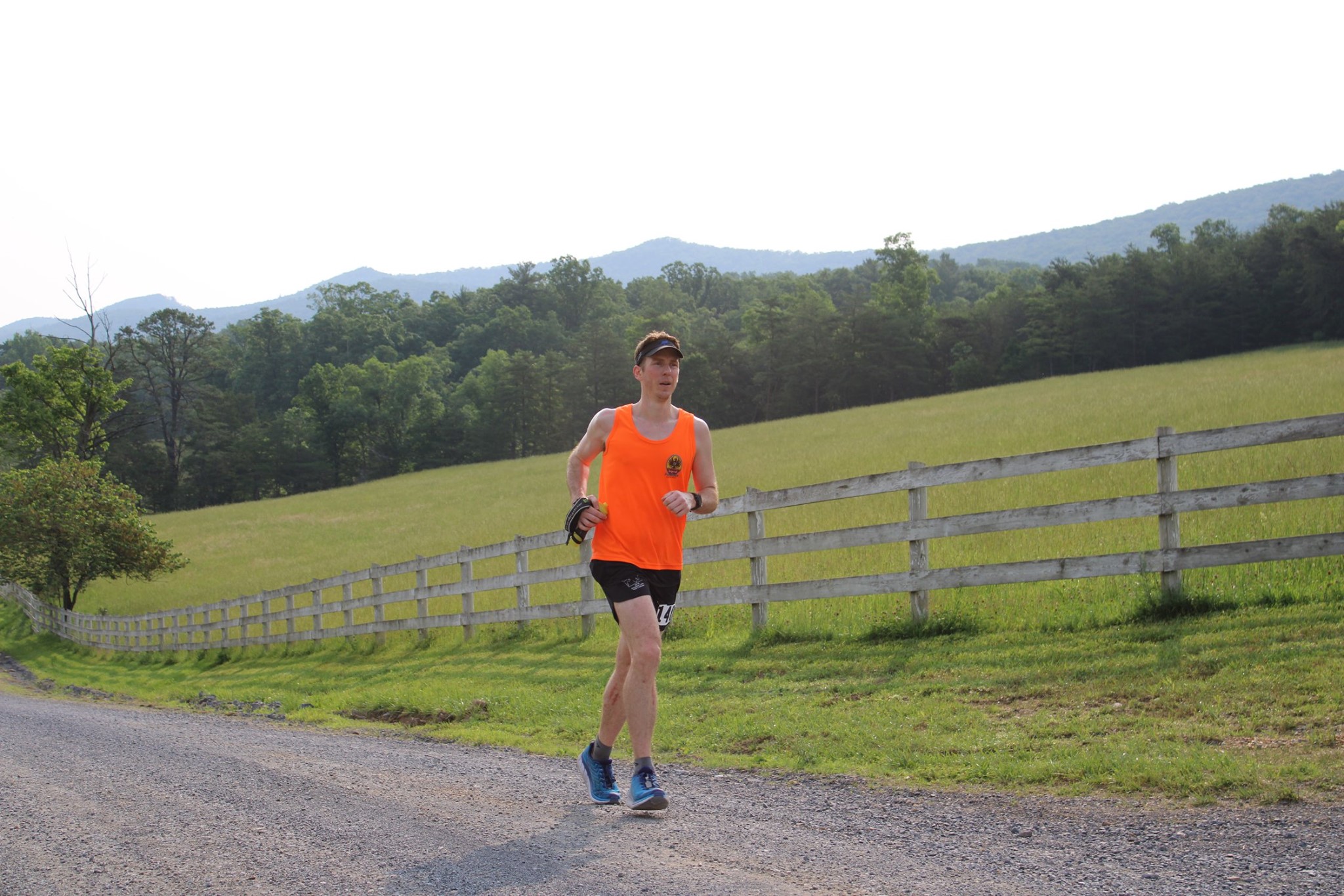 runner moving along gravel road in front of white farm fencing